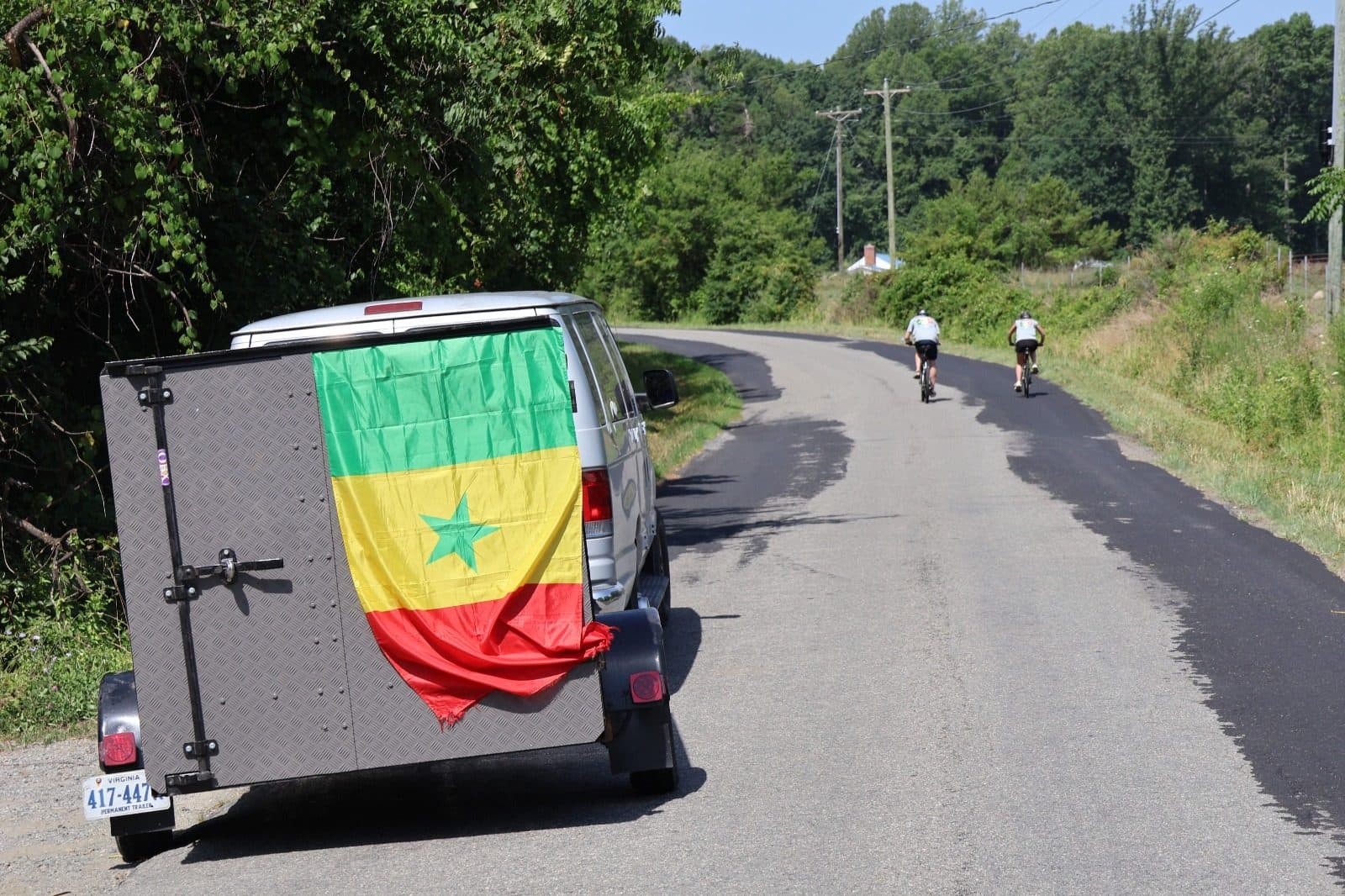 The support vehicle, decorated with a Senegalese flag, following riders down a country road